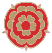 A stylised red and gold floral emblem with symmetrical, layered petals and small pointed details on the outer edge, resembling a Tudor rose inspired by the History of More House School.