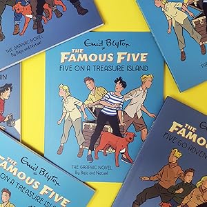 Five illustrated covers of Enid Blyton’s The Famous Five graphic novels are arranged on a yellow surface, with Five on a Treasure Island featured prominently in the centre.