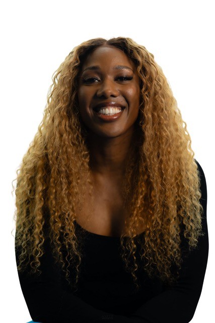 A woman with long, curly hair wearing a black top is smiling at the camera.