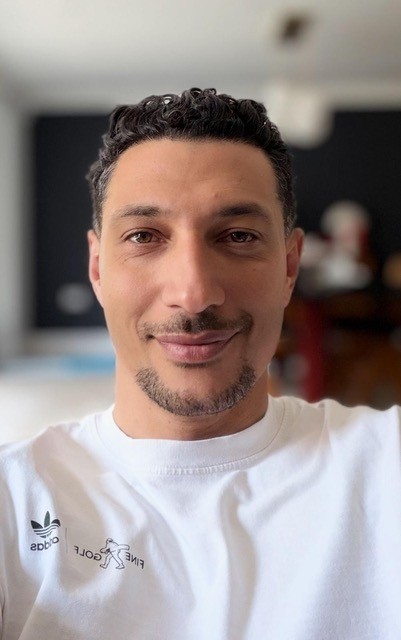 A man with short curly hair and a goatee smiles at the camera.