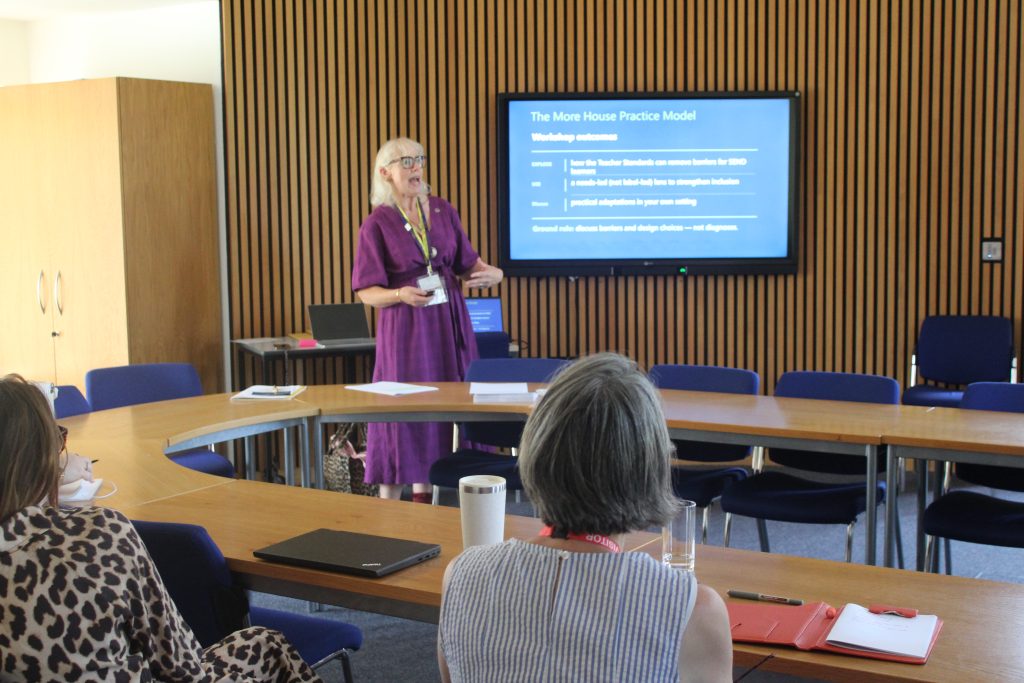 A woman in a purple dress presents in a conference room to a small group. A screen behind her displays The More House Practice Model workshop outcomes.